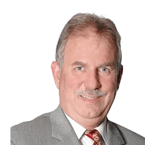 A middle-aged man with gray hair and a mustache is wearing a light gray suit, a white shirt, and a patterned red tie. He is smiling and facing the camera against a plain, white background.