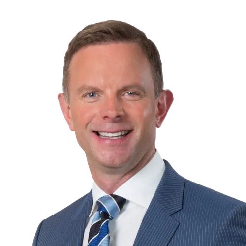 A smiling man with short brown hair wears a blue pinstriped suit, a white dress shirt, and a blue striped tie. He is photographed against a transparent background, facing forward with a friendly expression.