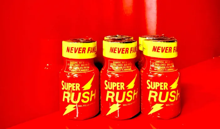 Three small red bottles labeled "SUPER RUSH" with yellow lightning bolts and caps that read "NEVER FAKE IT" in black text stand on a glossy red surface, with a red background, creating a vivid monochromatic effect.