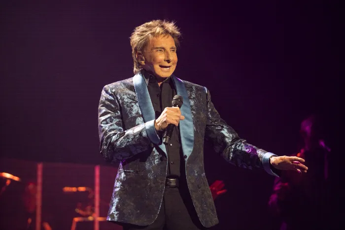 A man with light brown hair in a shiny blue patterned suit jacket and blue satin lapels holds a microphone and sings on stage at the 30th Annual The Chase, where $2.3 million was raised celebrating DAP Health’s 40th Anniversary.