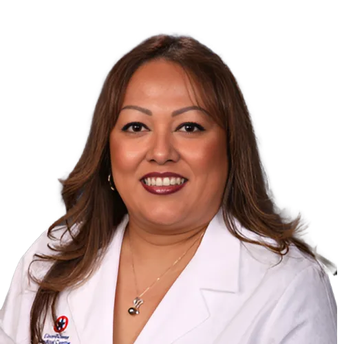 A woman with long, brown hair smiles at the camera. She is wearing a white lab coat, a gold necklace, and dark lipstick. The background is plain and unobtrusive, focusing attention on her professional attire and friendly expression.