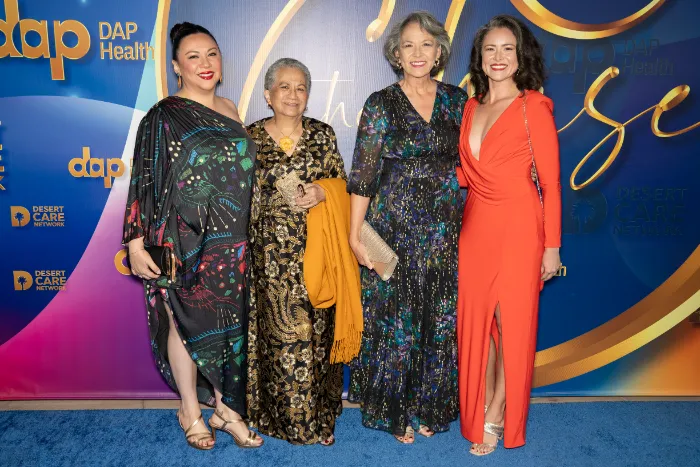 Four women stand together on a blue carpet at the 30th Annual The Chase, celebrating DAP Health’s 40th Anniversary and $2.3 Million Raised. They wear elegant dresses in bold colors, with a backdrop of vibrant logos and event graphics.