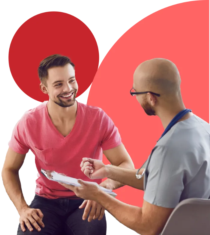 A smiling man in a pink T-shirt sits and talks with a healthcare professional in scrubs holding a clipboard. Both appear engaged and friendly. The background features large overlapping red and pink circles.