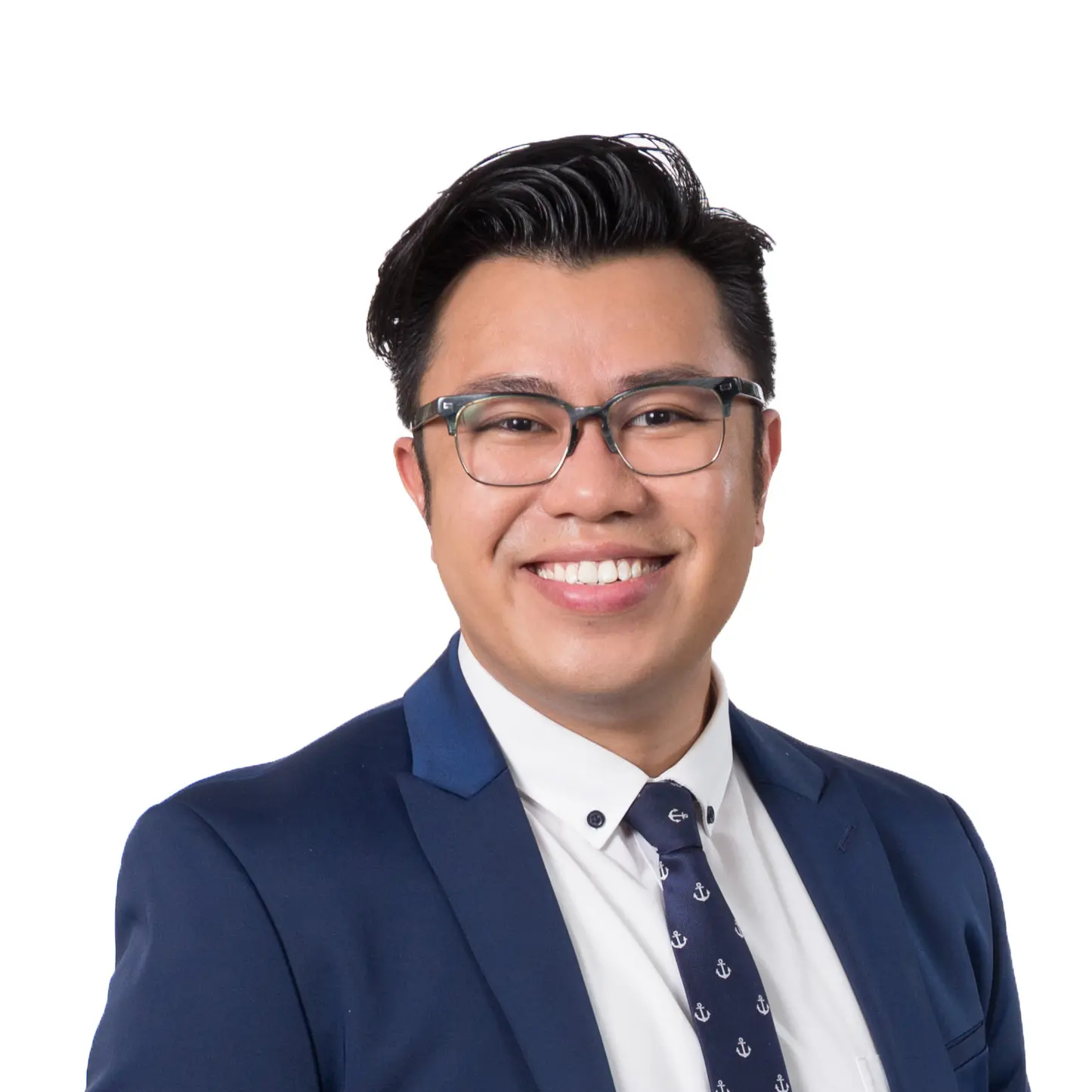 A man with short, dark hair and glasses smiles at the camera. He is wearing a navy blue suit, a white shirt, and a navy tie with small white anchor patterns. The background is plain white.
