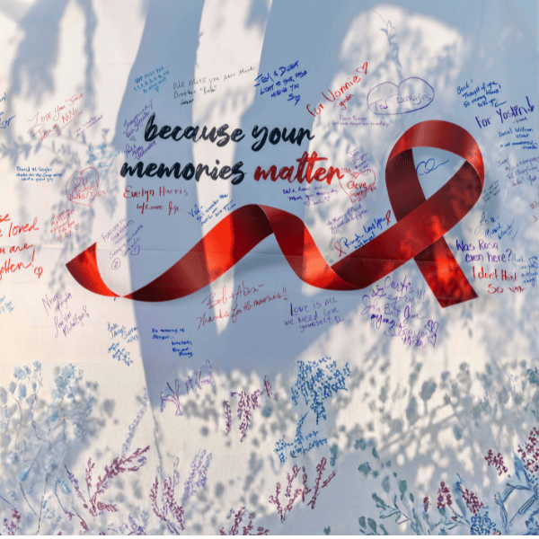 A white wall displays a large red awareness ribbon and the words "because your memories matter," surrounded by handwritten colorful messages of love and remembrance. Soft shadows of leaves and flowers fall across the wall, adding a gentle, peaceful atmosphere.