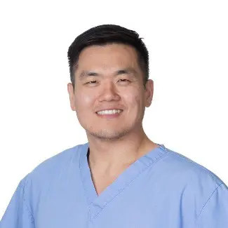 Daniel Jo, a smiling man with short black hair, wears light blue medical scrubs. He stands against a plain white background, facing forward and appearing professional and approachable.