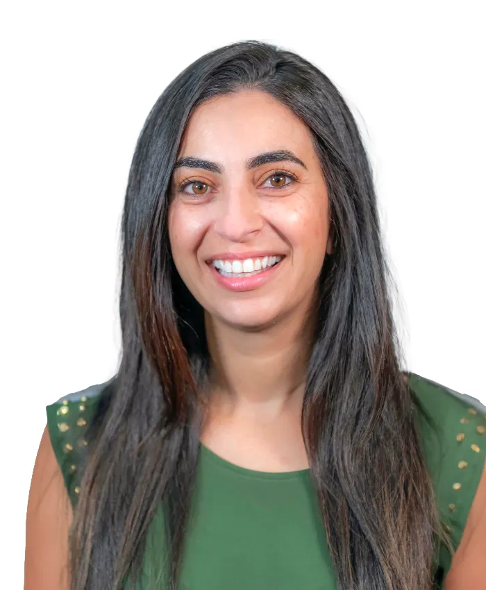 A woman with long, straight dark hair smiles at the camera. She is wearing a green sleeveless top with gold studs on the shoulders. The background is plain white, making her the clear focus of the image.