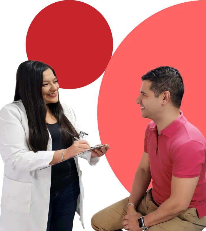 A smiling woman in a white lab coat holds a clipboard and writes while talking to a seated man in a pink shirt. Both appear engaged and friendly. The background features large red and pink circles.