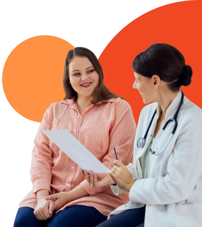 A doctor in a white coat with a stethoscope shows a document to a smiling woman in a pink striped shirt. They are seated and appear to be having a friendly conversation, with abstract orange shapes in the background.