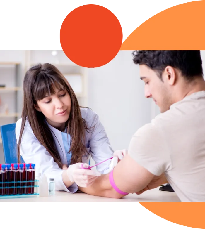 A female healthcare worker draws blood from a man's arm using a needle. She wears a white coat and gloves. The man sits with his arm extended and a purple tourniquet on his bicep. Blood samples are in test tubes nearby. The scene takes place in a clinical setting.