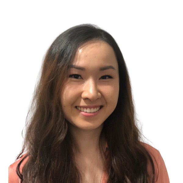 A young woman with long, wavy dark hair smiles at the camera. She has fair skin, straight eyebrows, and is wearing a peach-colored blouse. The background is plain white, putting full focus on her face and upper shoulders.